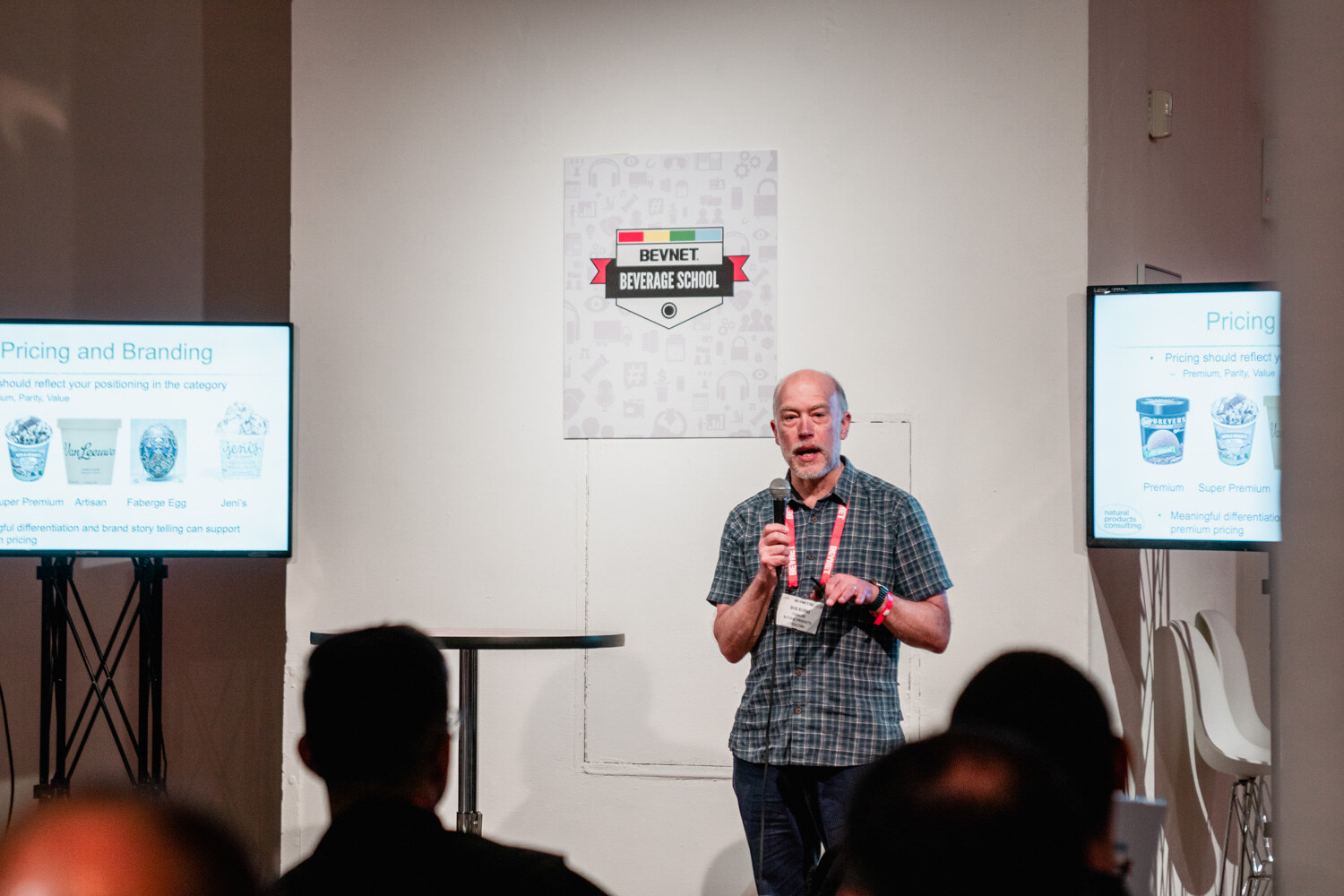 A man in a plaid shirt speaks into a microphone between two screens titled Pricing and Branding.