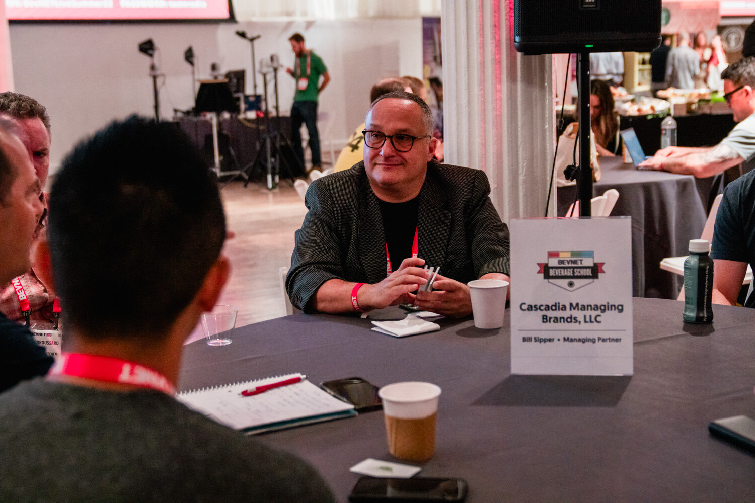 A man with glasses sits at a round table with a notebook and a table card reading Cascadia Managing Brands, LLC.