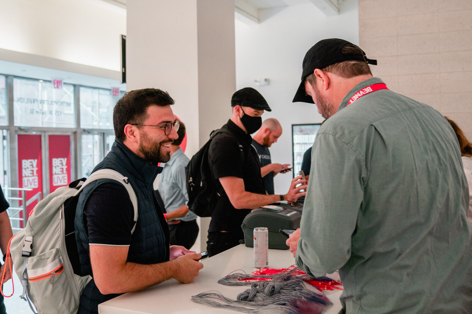 A man with glasses smiles at a white registration counter while others check in beside him.