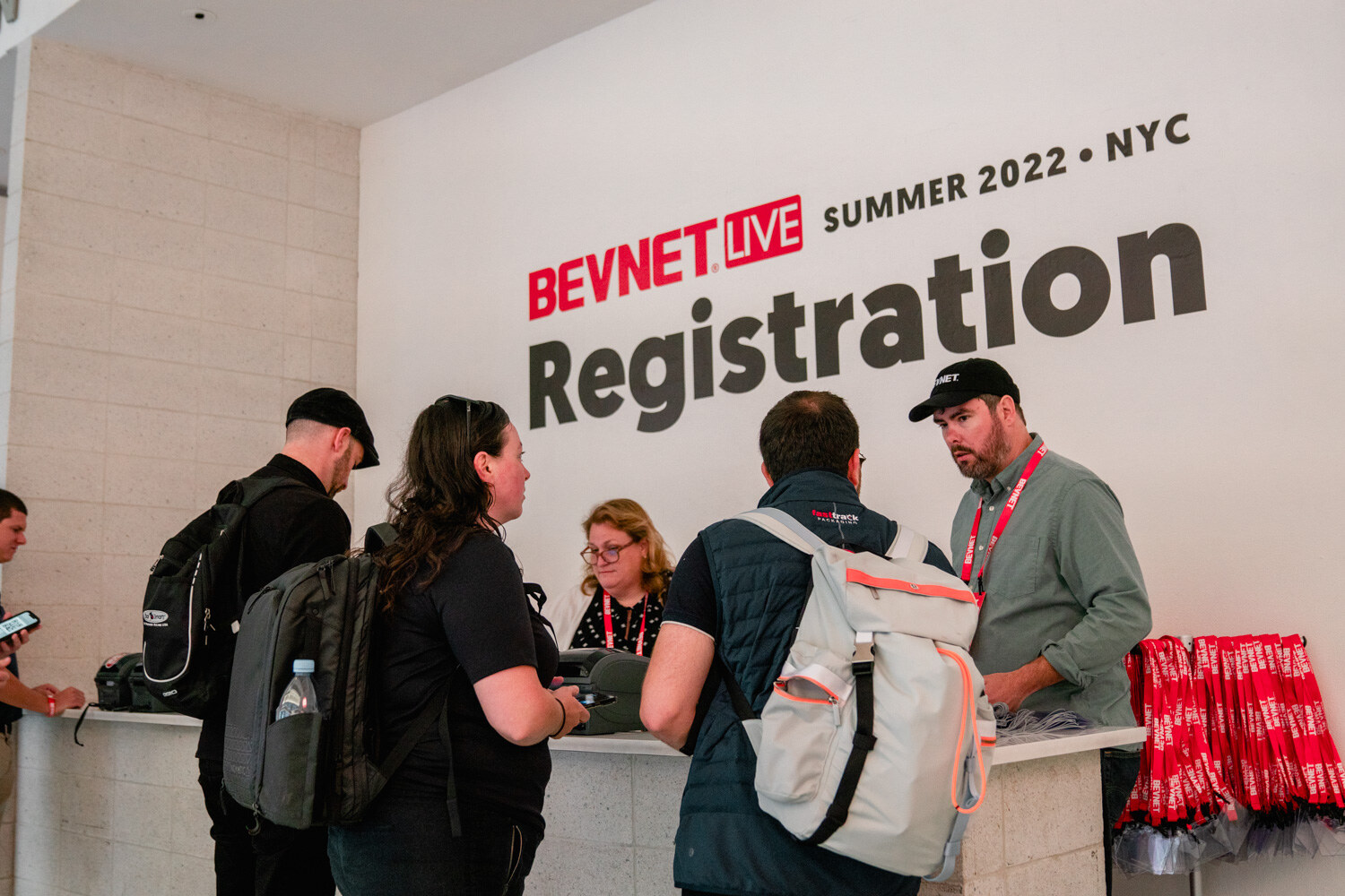 A group at a white counter below a sign reading BevNET Live Summer 2022 NYC Registration, with red lanyards on the counter.
