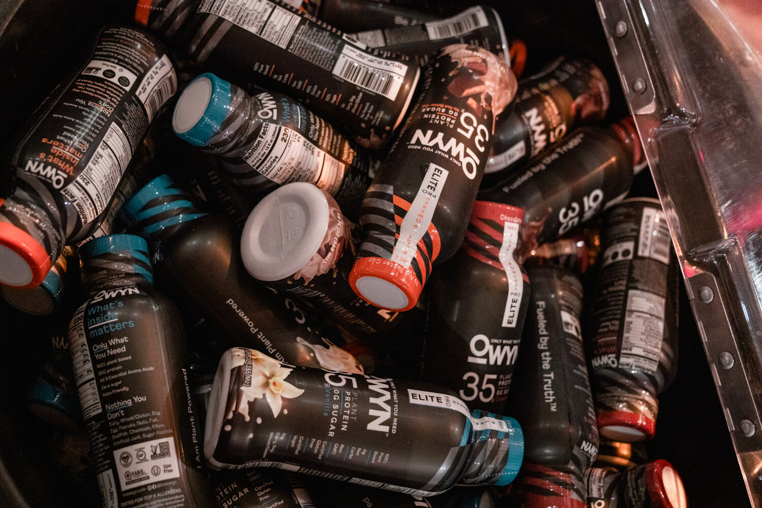 Overhead view of dark Owyn 35 protein shake bottles piled together, some with blue caps.