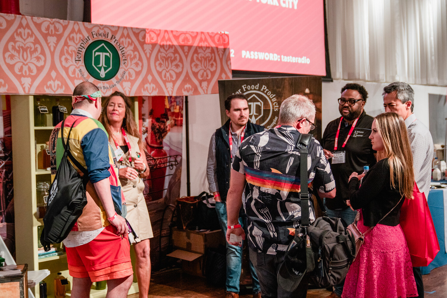A crowd of attendees talk near a pink patterned booth topped with a Templar Food Products sign, a BevNET Live screen above.