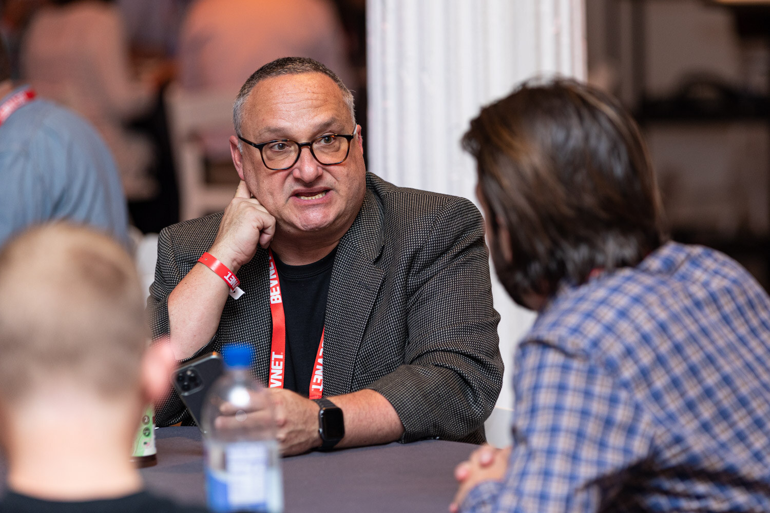 A man with glasses and a red BevNET lanyard speaks at a table, with a water bottle in the foreground.