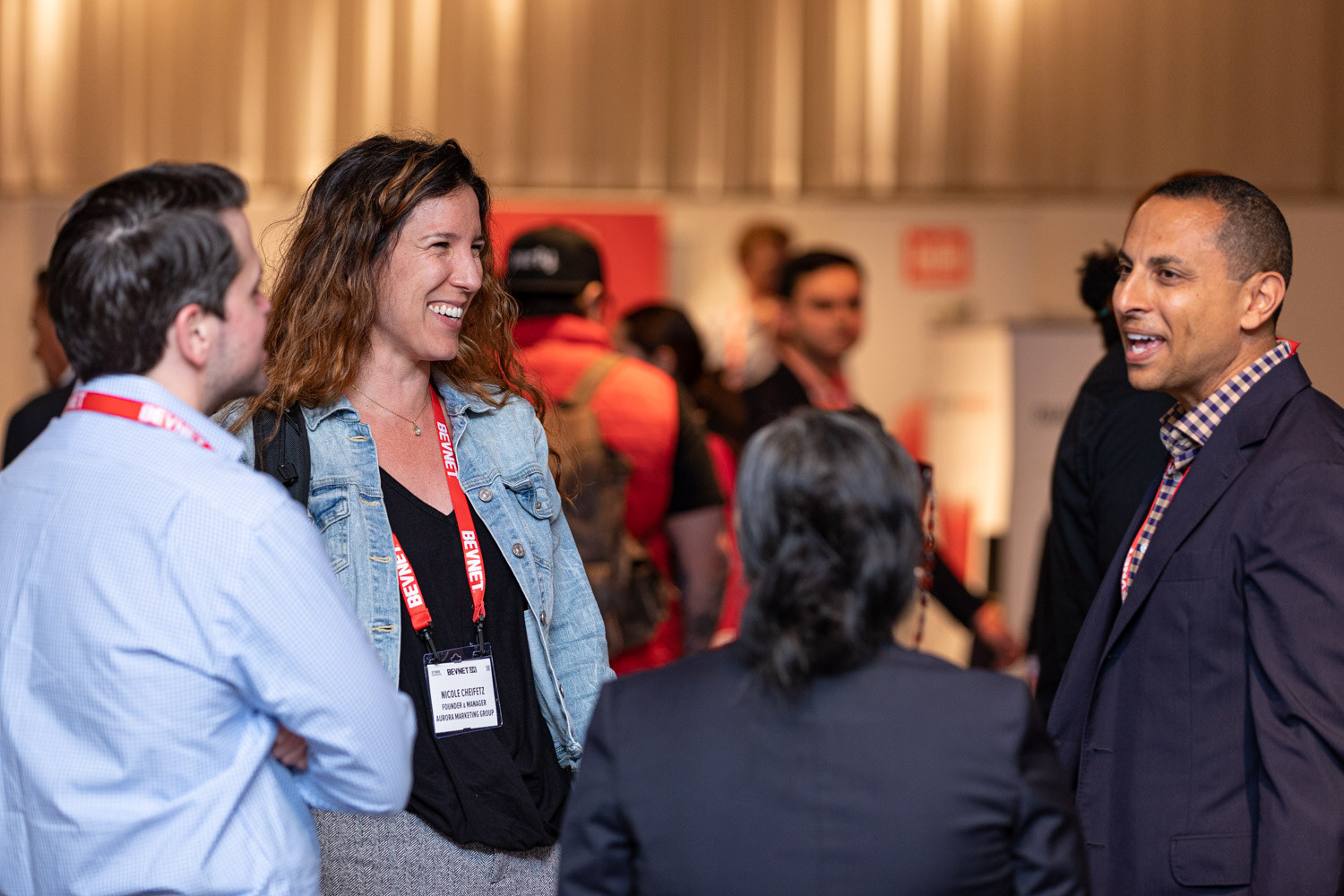 A woman in a denim jacket and two men in lanyards talk and smile together in the lunch area.