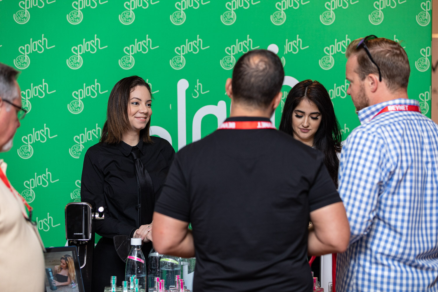 A group of people at a booth with a green backdrop covered in Splash logos, with drinks on the table.