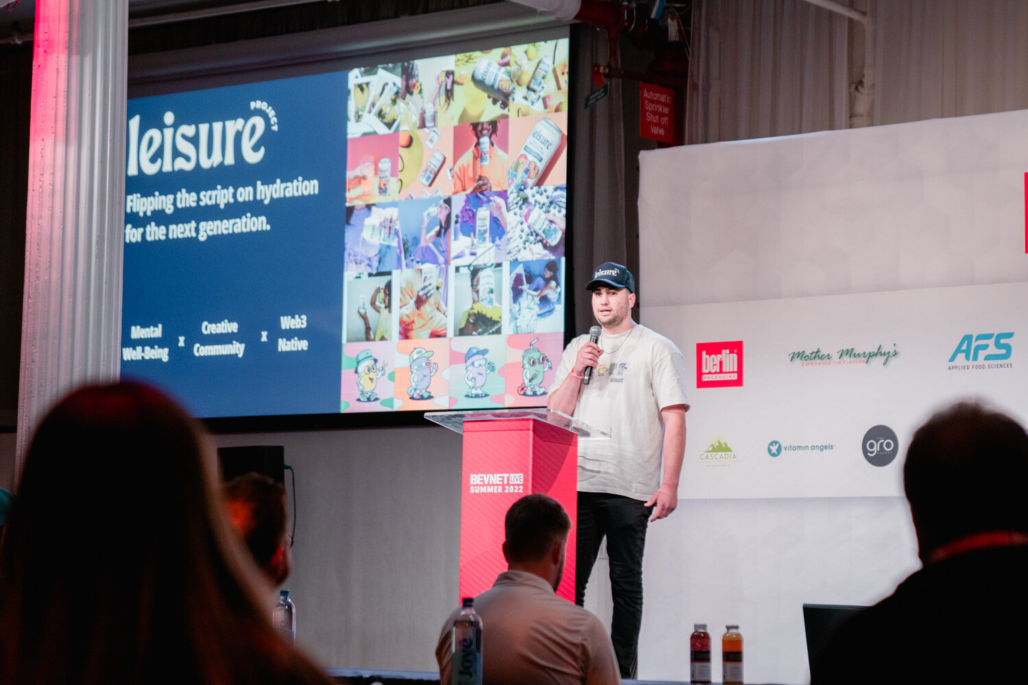 A man in a navy cap and cream shirt stands at a red podium with a blue Leisure slide on the screen.