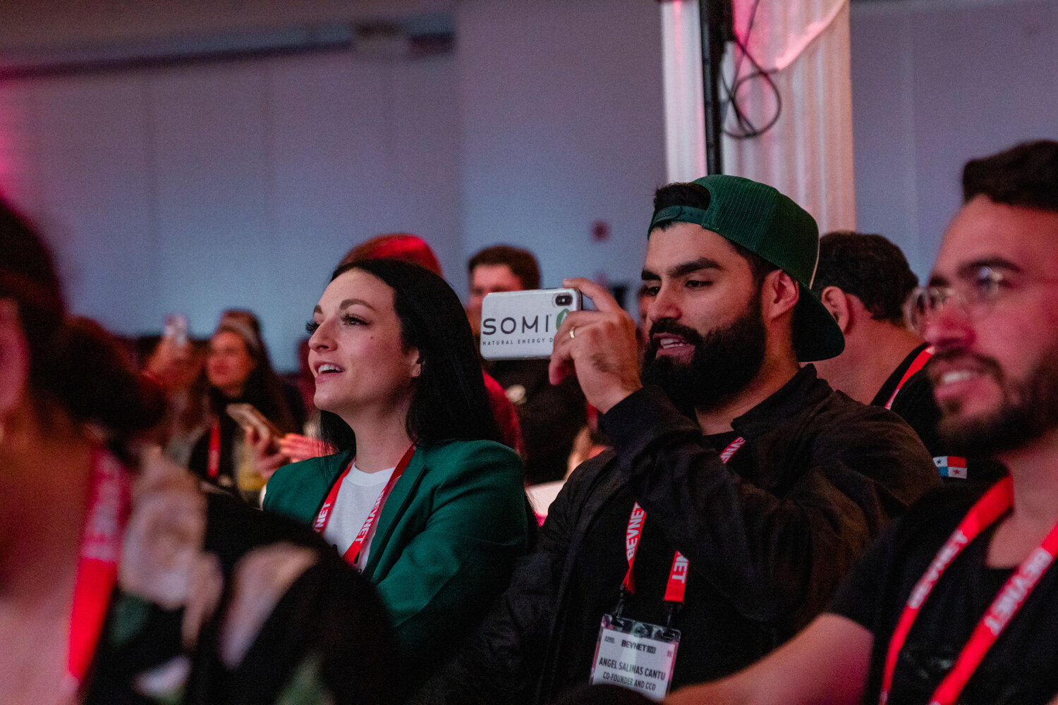 Several attendees with red BevNET lanyards look toward the stage, one holding up a phone.