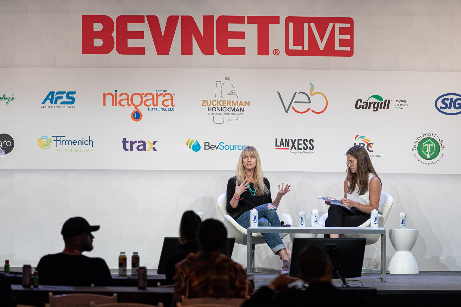 Two women seated on a stage in front of a BevNET Live backdrop, one gesturing while the other holds papers.