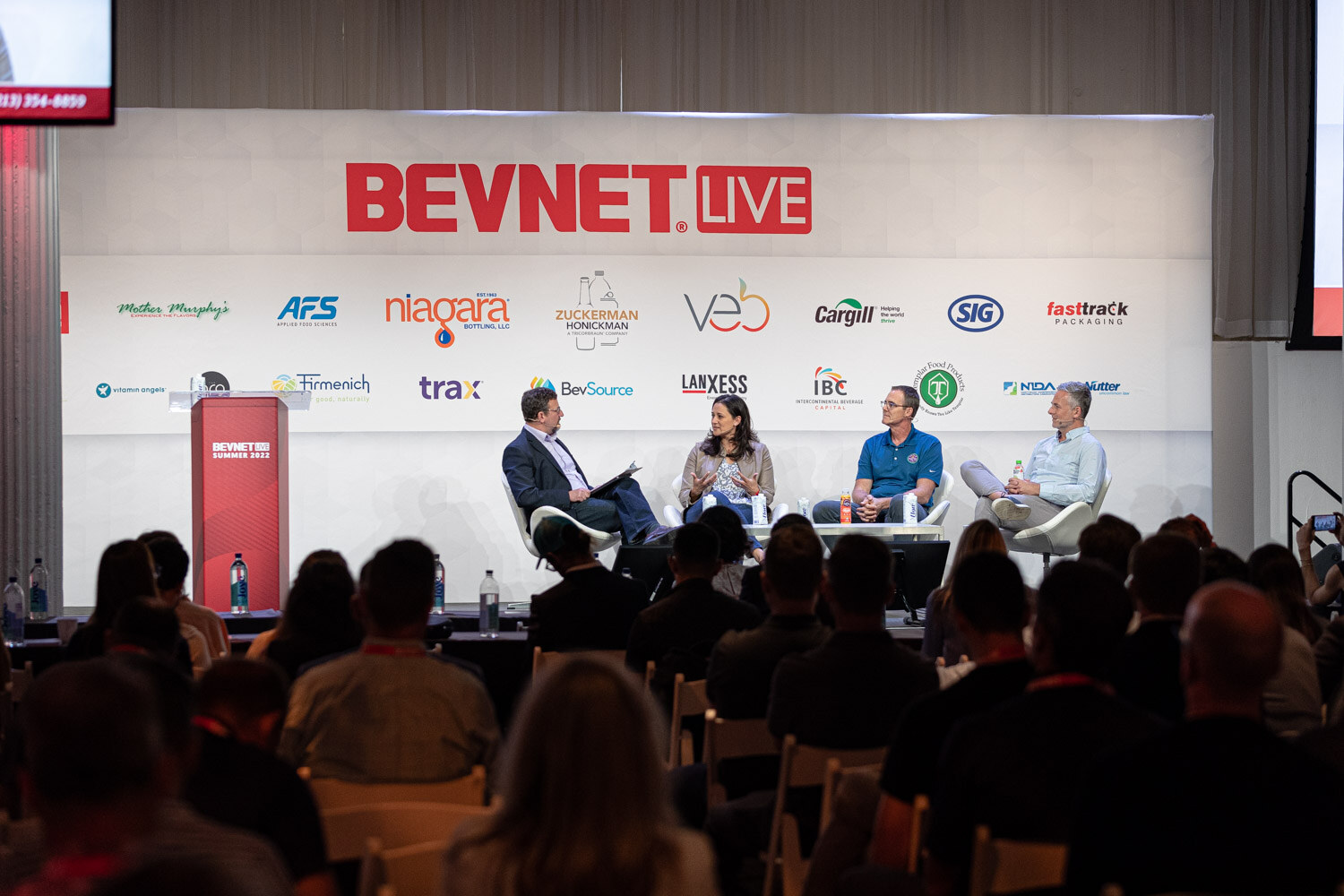 Wide view of four people seated on a stage under the BevNET Live sign, attendees' heads in the foreground.