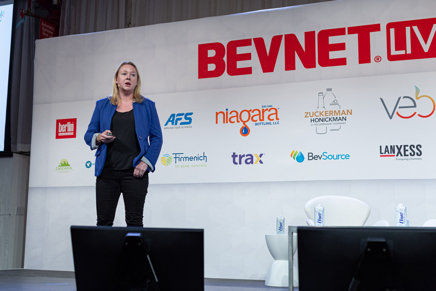 A woman in a blue blazer and black pants stands holding a clicker below the BevNET Live sign.