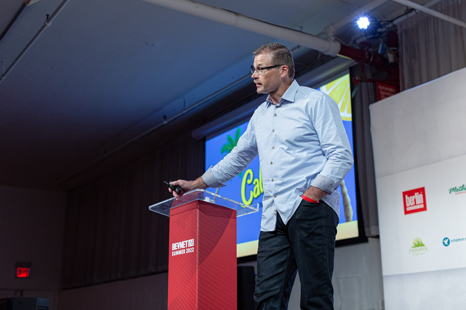 A man in a light blue shirt and glasses stands next to a podium holding a clicker with a Calypso slide partly visible behind him.