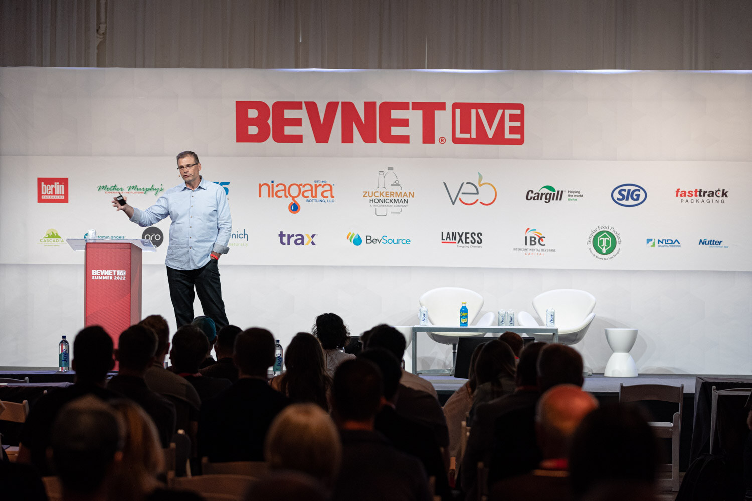 Wide view of a man in a light blue shirt on stage below a BevNET Live sign, with audience members in the foreground.