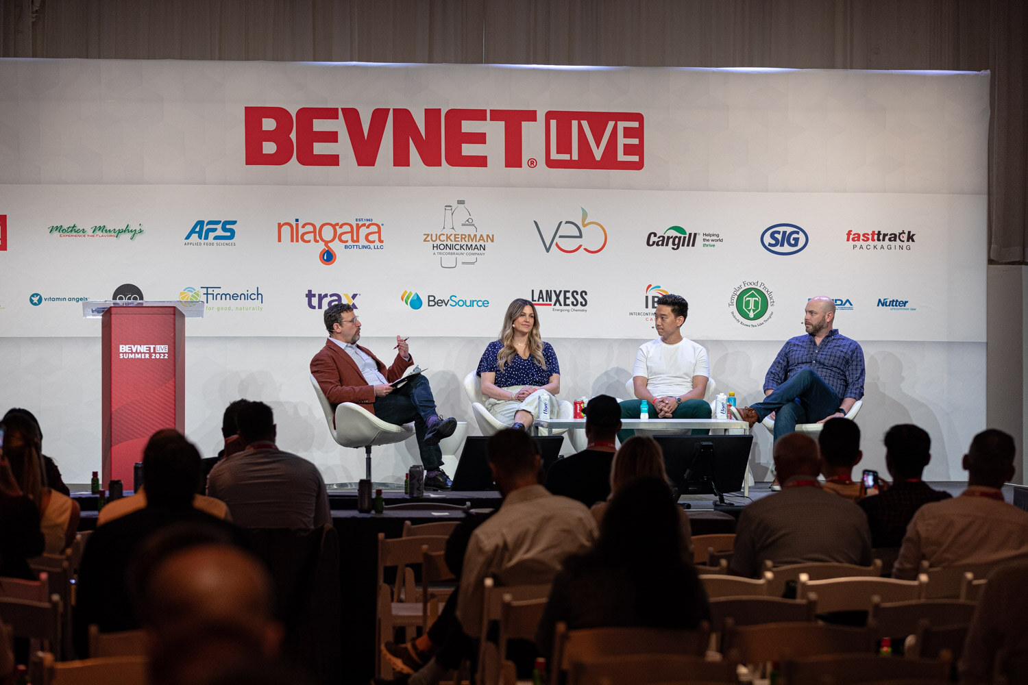 Wide view of four people in white chairs below the BevNET Live sign with the audience in the foreground.