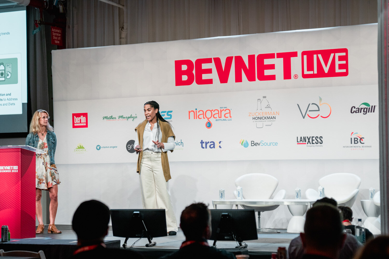 Two women stand on stage below the BevNET Live sign, one at the left near the podium and one at center with a clicker.