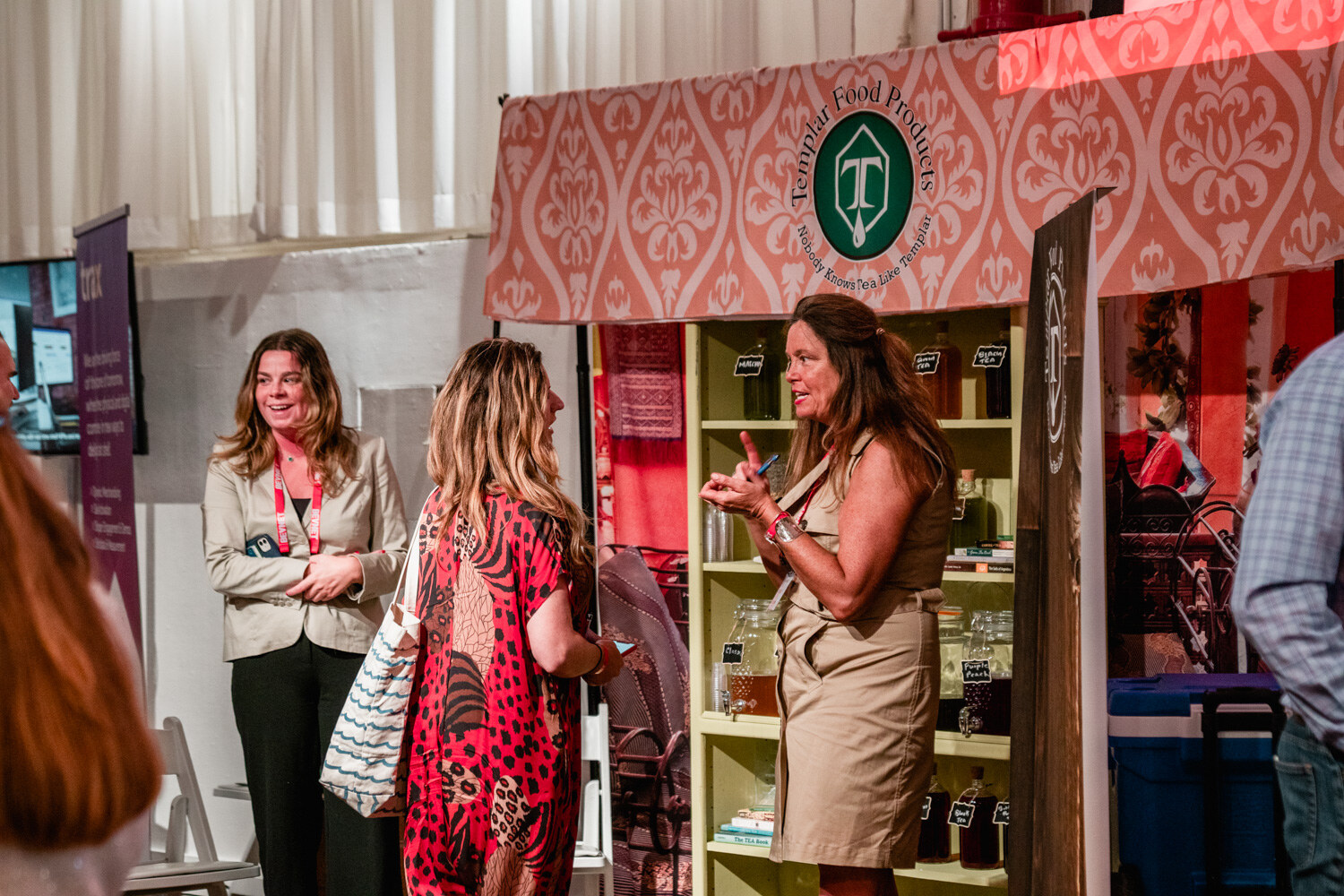 Three women in conversation in front of a pink patterned booth topped with a Templar Food Products logo.