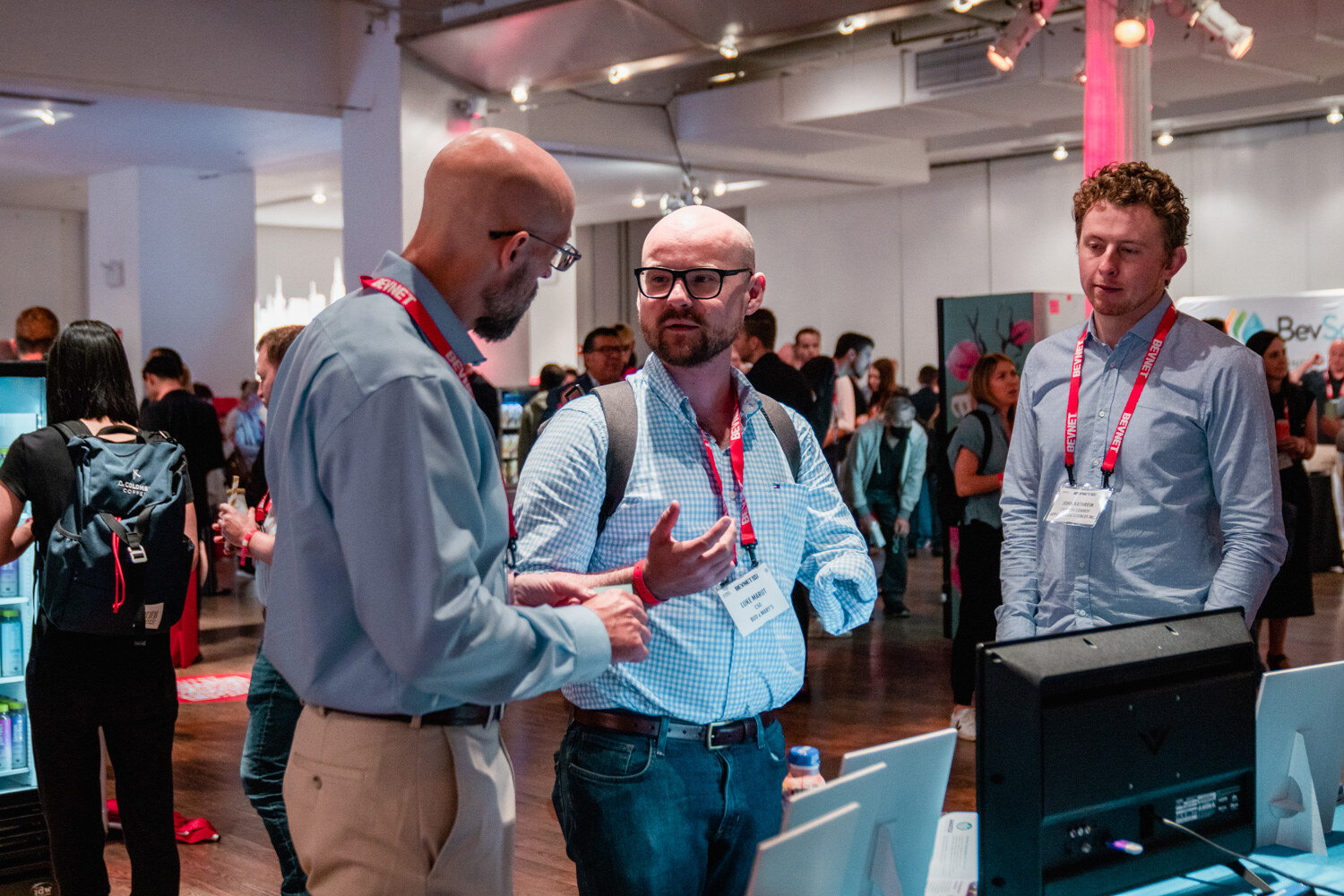 A bald man in glasses, a man in a checked shirt and a man in a light blue shirt with lanyards stand together in the hall.