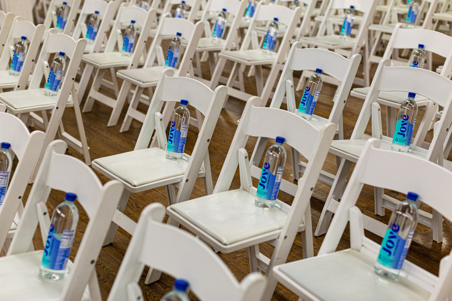 Rows of white folding chairs with a bottle of Joye water on each seat.