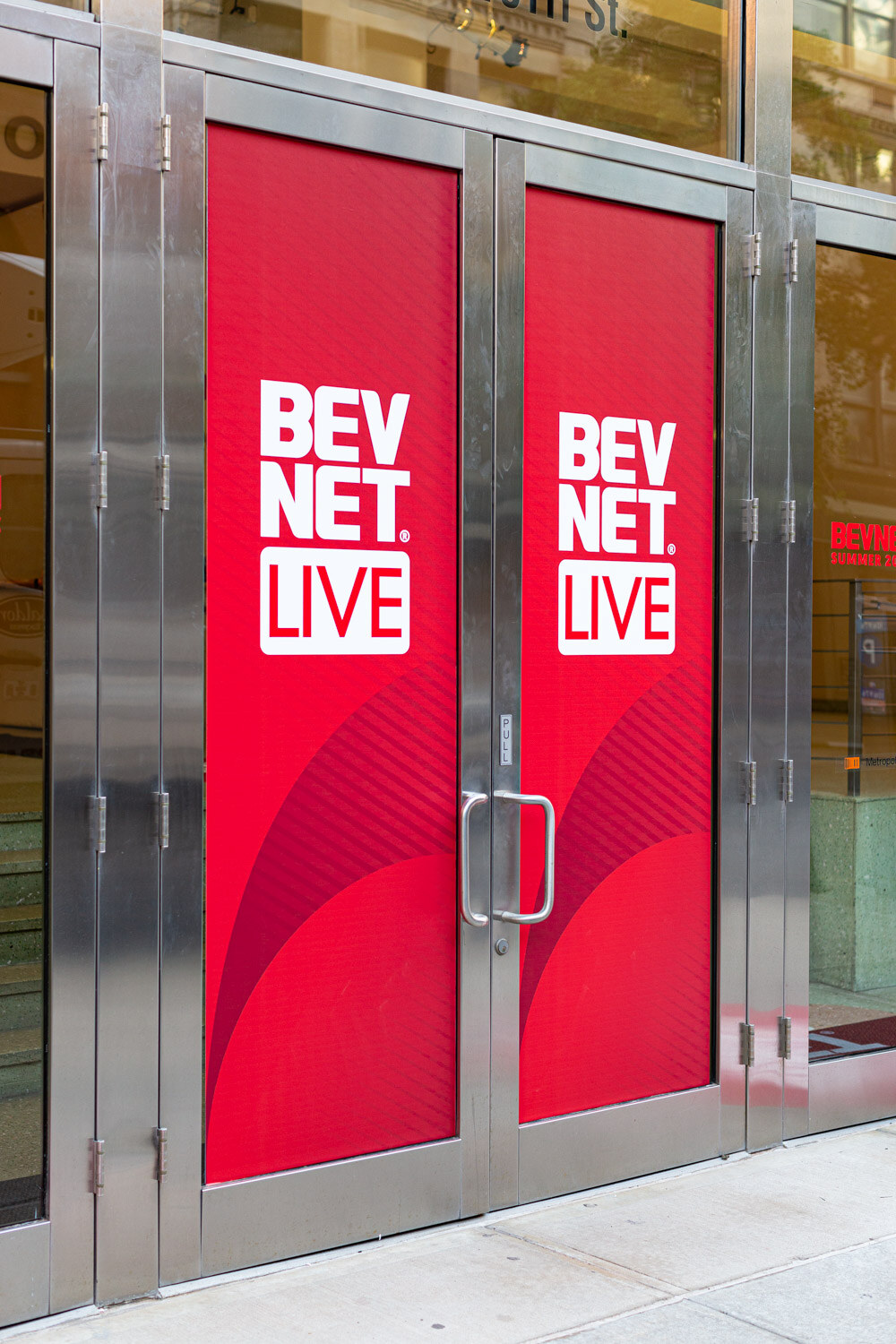 A pair of silver framed glass doors covered with red decals reading BevNET Live.