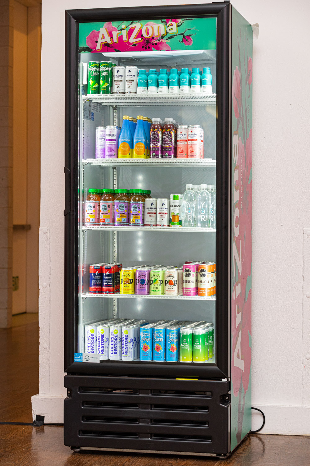 A black glass-door cooler with Arizona branding filled with canned and bottled drinks on lit shelves.