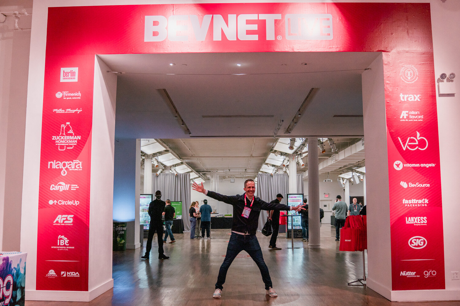 A man with outstretched arms stands in the doorway of a tall red arch labeled BevNET Live with sponsor logos down both sides.