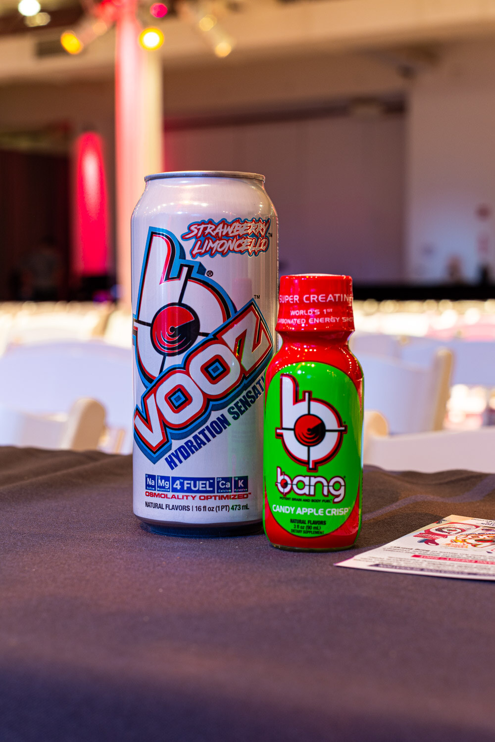 A can of Vooz Hydration Sensation Strawberry Limoncello beside a green bottle of Bang on a black tablecloth.