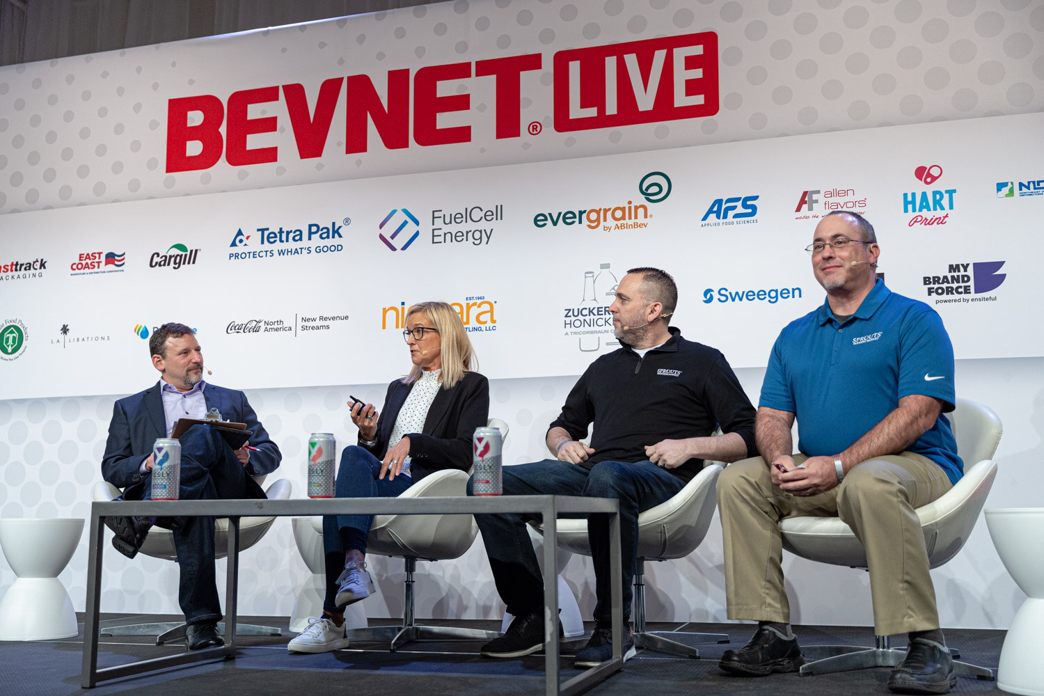 Wide shot of four people seated on a stage under the BevNET Live logo, with a slide of store shelves on the screen at right.