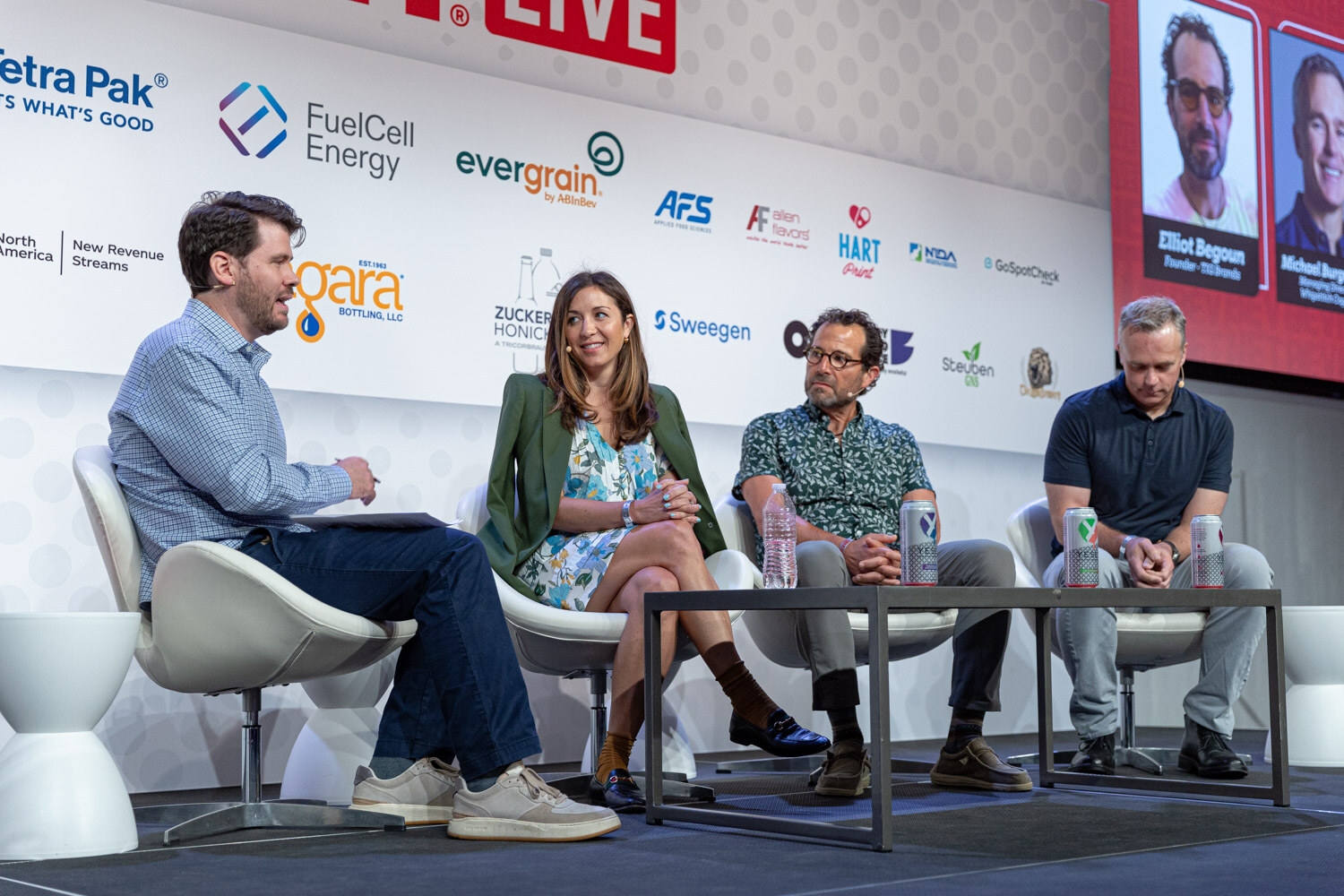 Wide shot of four people seated on a stage in front of the BevNET Live backdrop with portraits of two panelists on the screen at right.