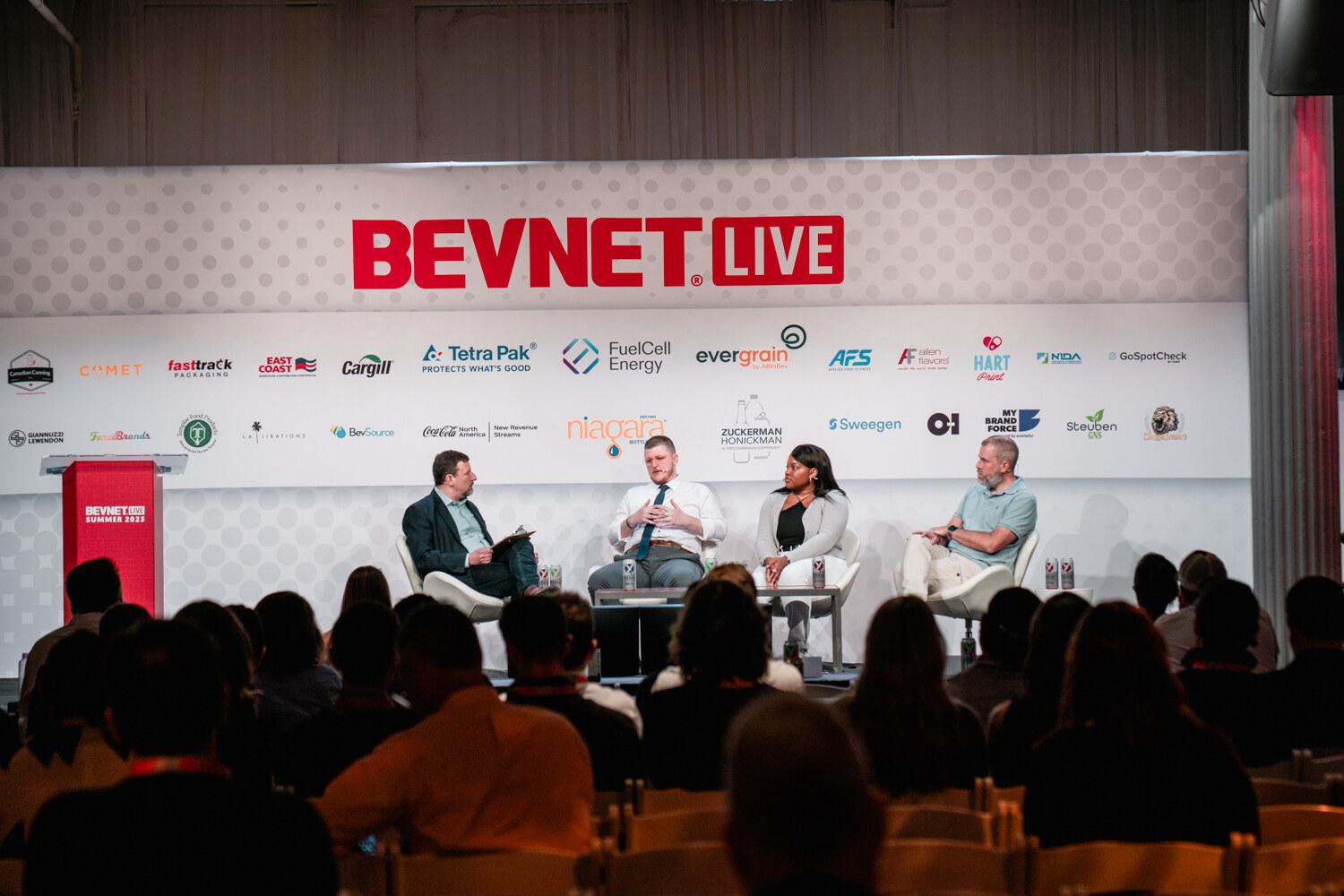 Wide shot from the audience of four seated panelists on a stage with the BevNET Live logo, a podium at left and rows of attendees in the foreground.