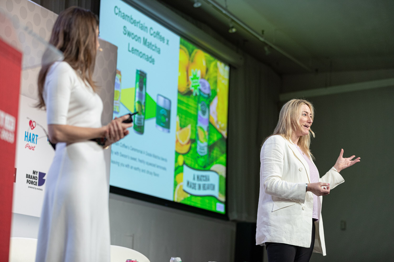 Two women in white outfits stand on opposite sides of a screen showing a green and yellow slide about a matcha lemonade collaboration.