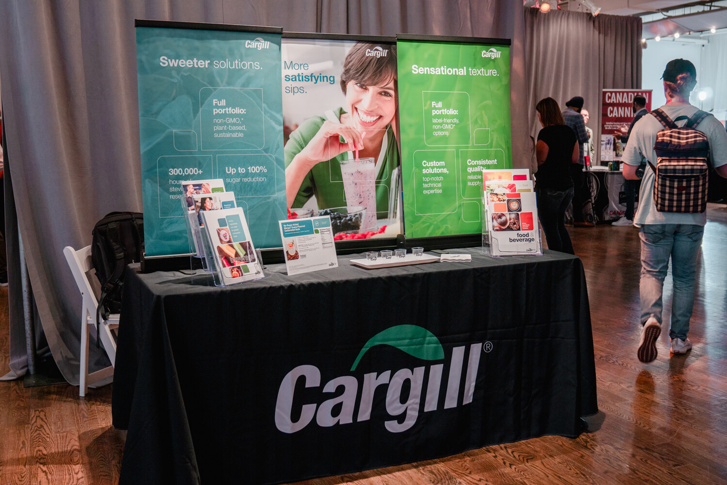 A black draped table with a Cargill logo stands in front of three green and teal banners about sweeter solutions and sensational texture.