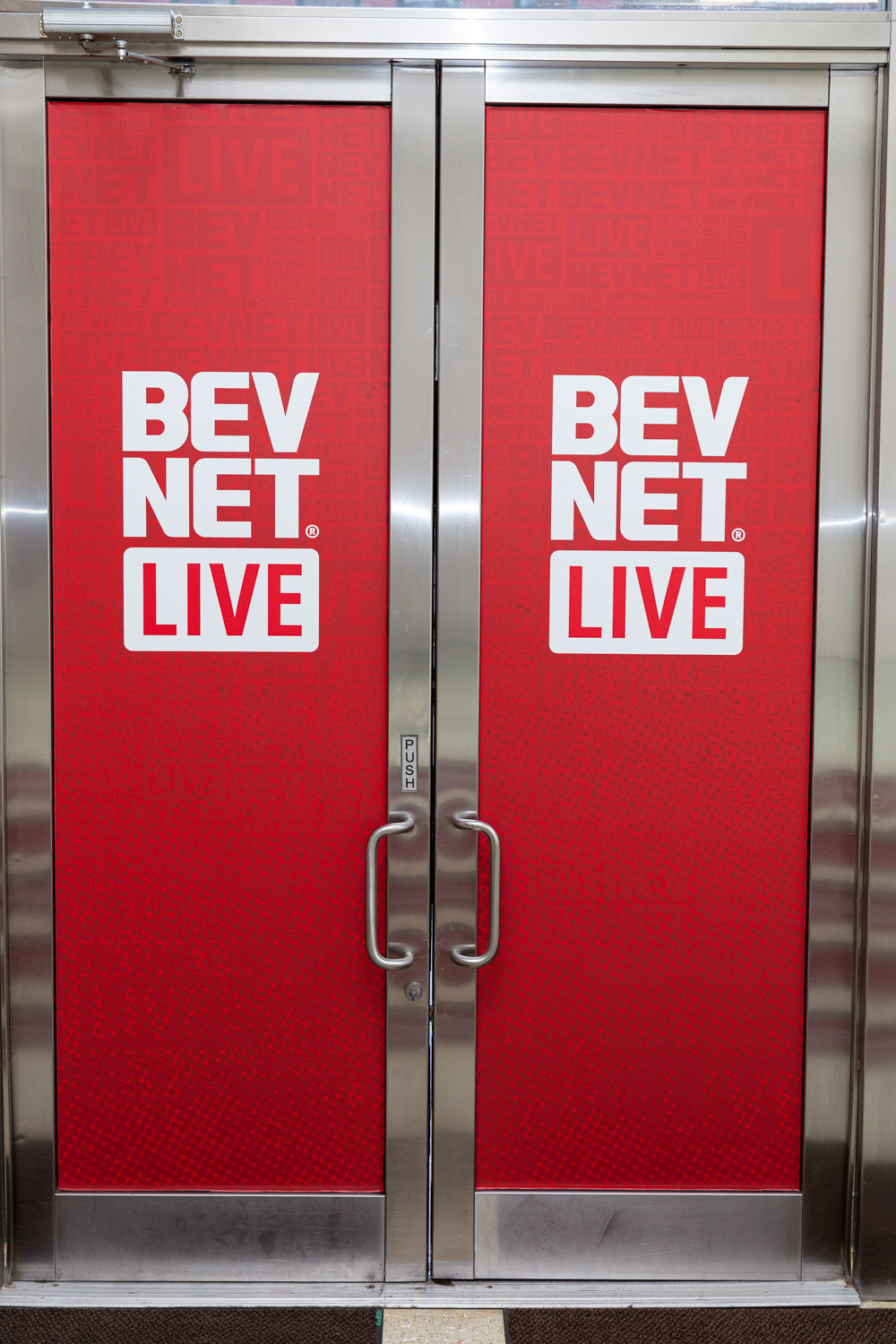 A pair of steel-framed double doors wrapped in red vinyl with the white BevNET Live logo repeated twice.