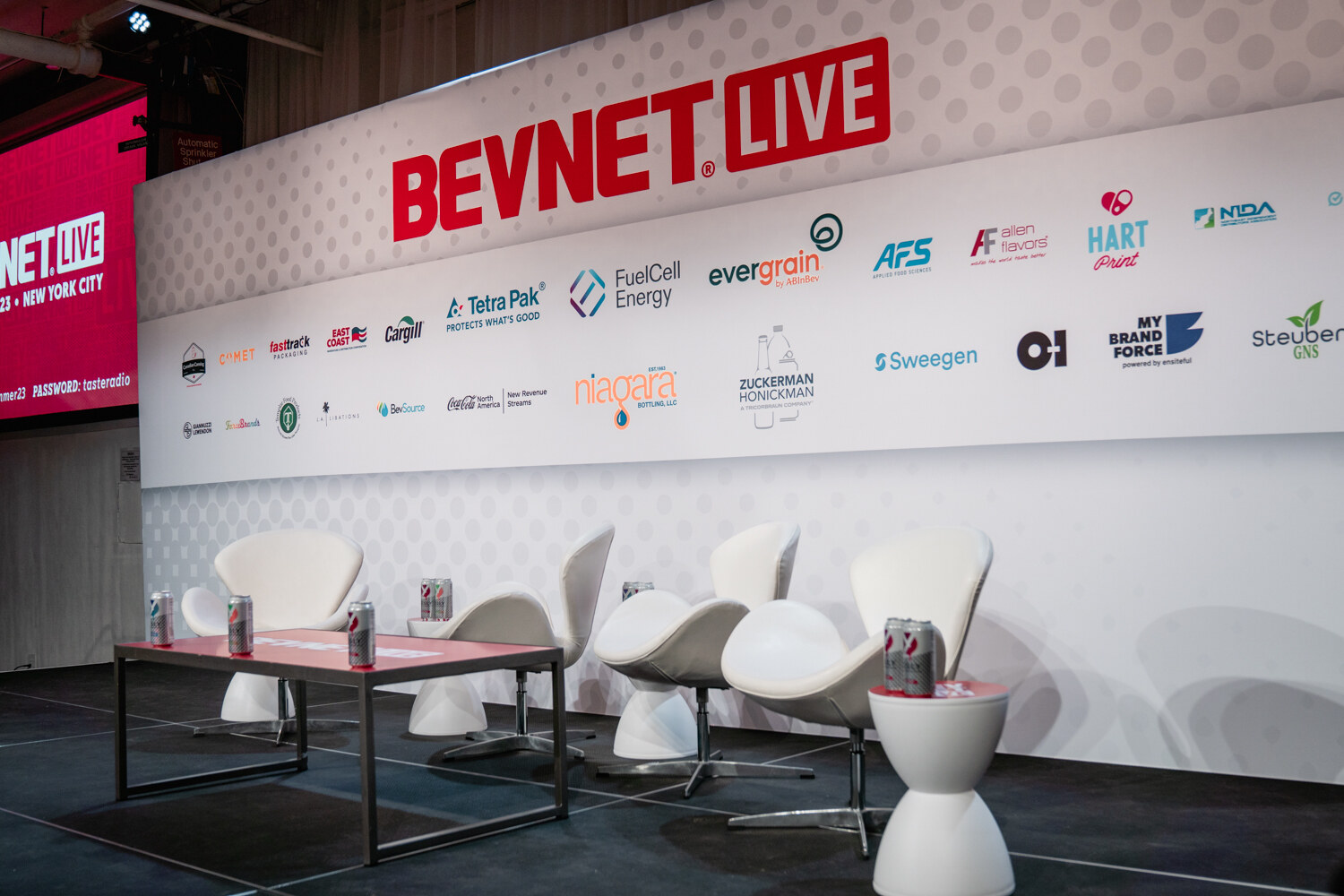 White swivel chairs and a low table with cans sit on the stage in front of the BevNET Live backdrop with sponsor logos.