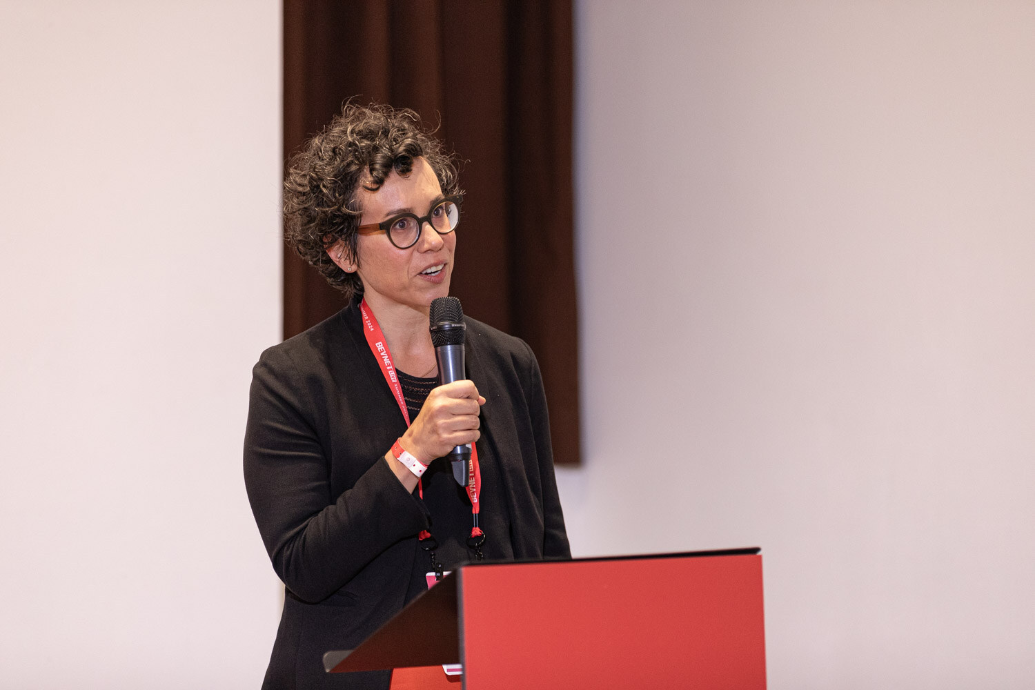 Moderator in a black blazer holds a microphone at the Beverage School podium.