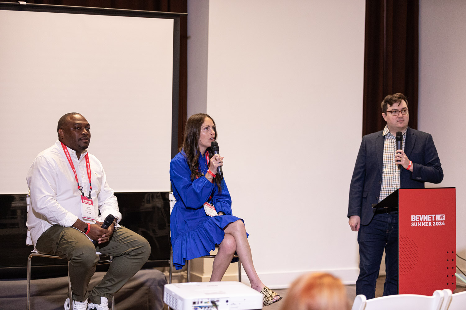 Moderator and two seated panelists in front of a projection screen at Beverage School.