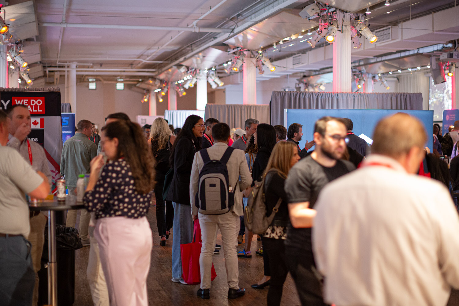 Crowded happy hour floor with attendees talking between exhibitor booths.