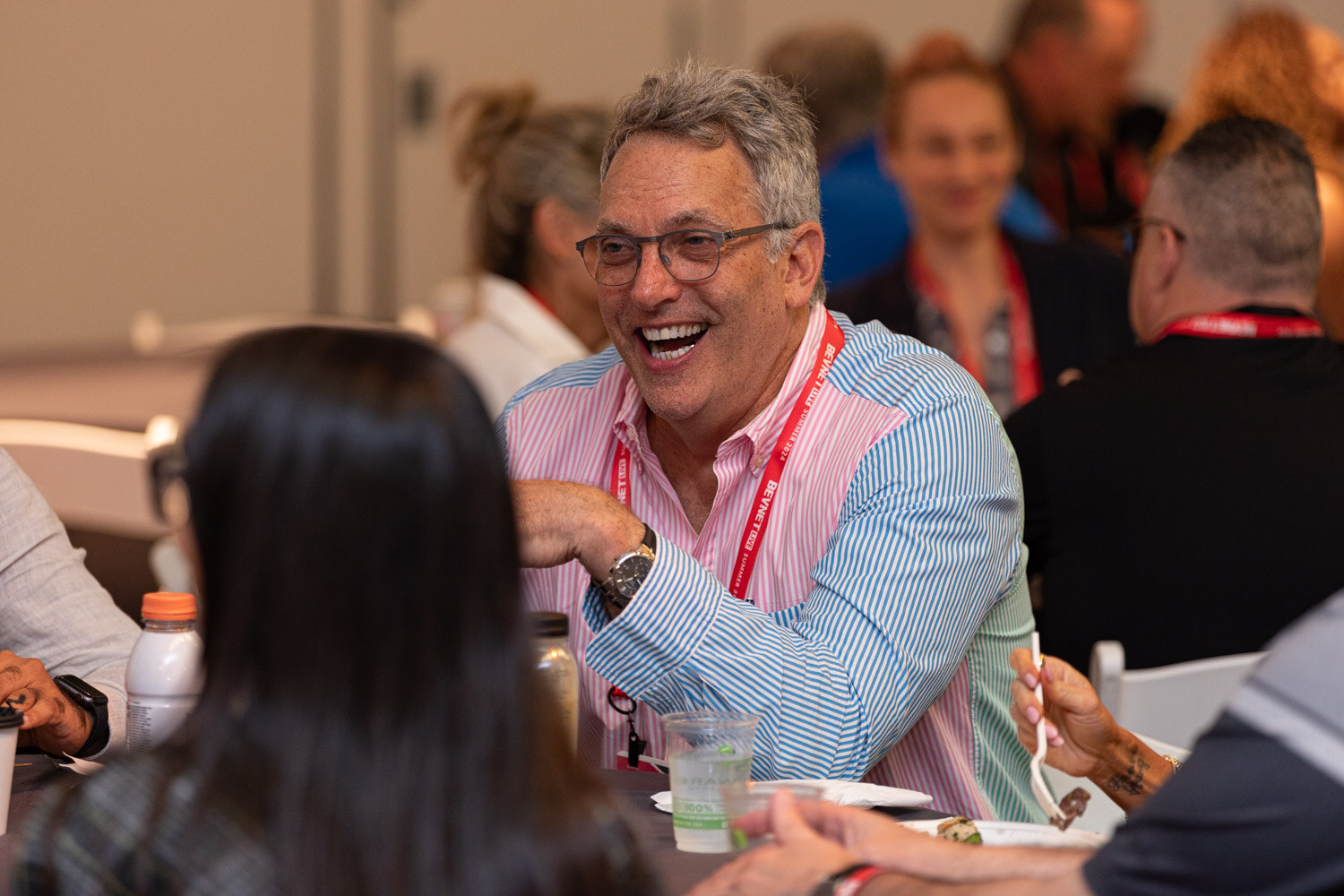 Attendee in a pink-and-blue striped shirt laughs at a lunch table.