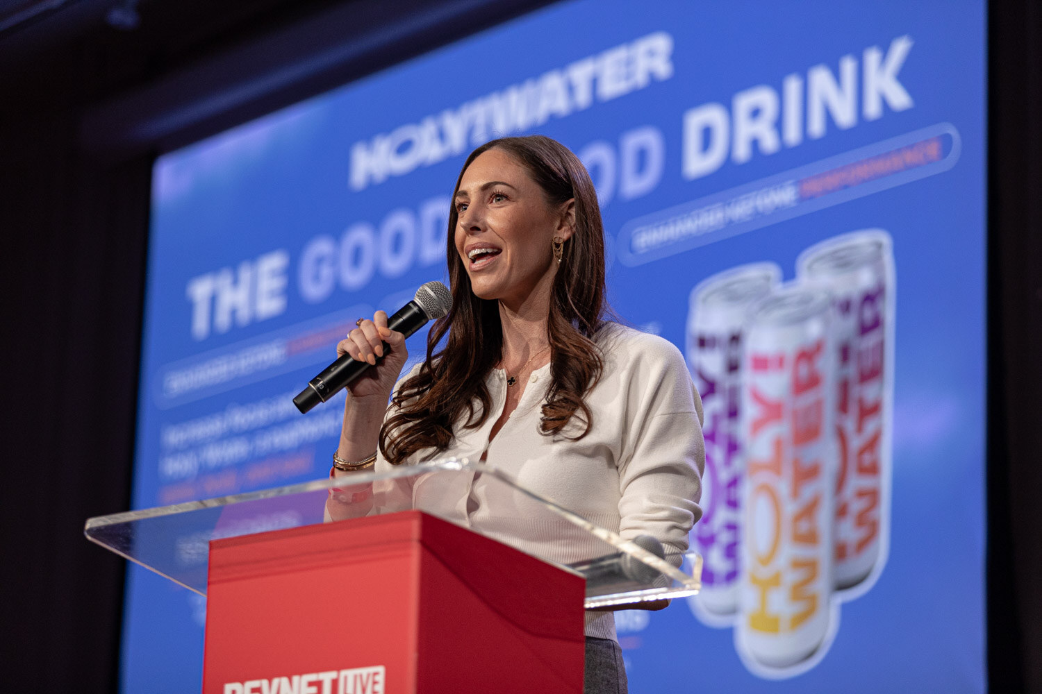 Contestant in a white blouse speaks at the podium in front of a Holy Water slide.