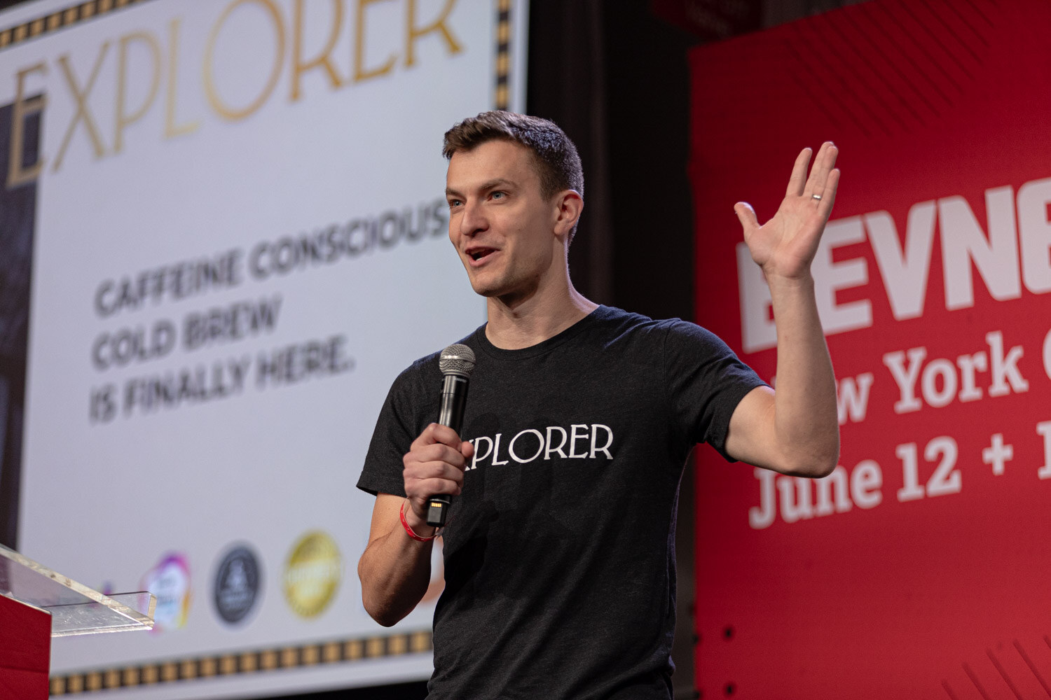 Contestant in an Explorer t-shirt gestures during a pitch about caffeine conscious cold brew.