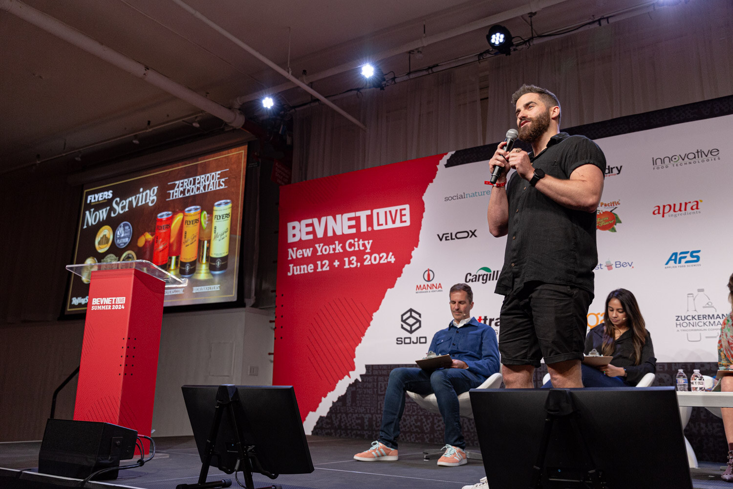Wide view of a contestant pitching on stage while the judges sit at the side.