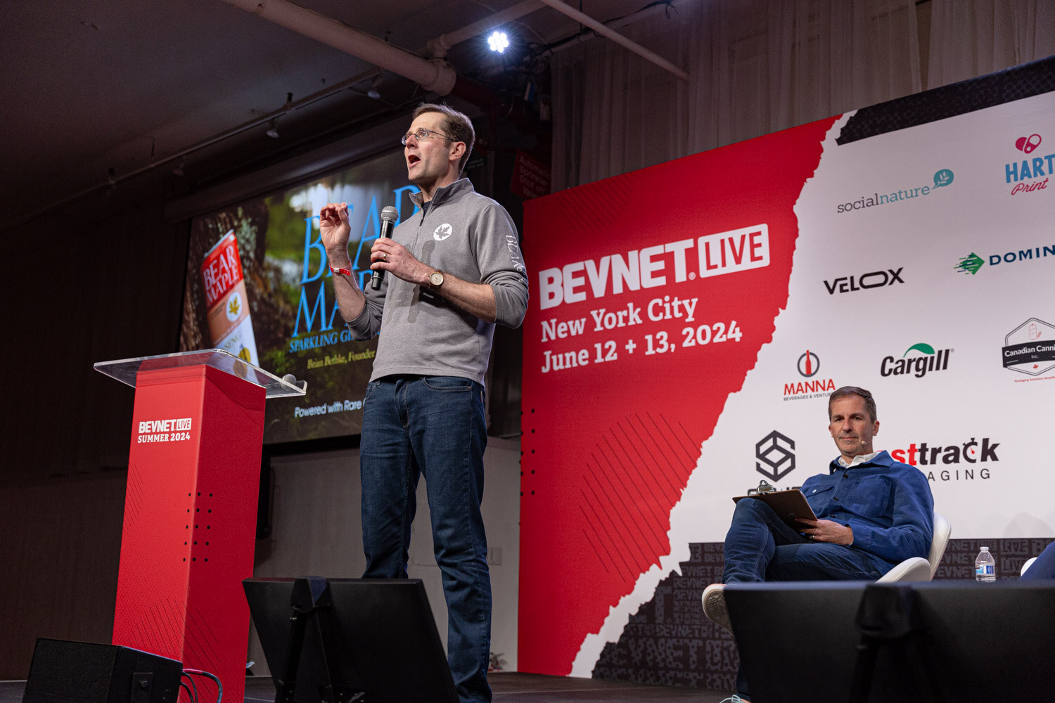 Contestant at the podium with a judge seated on stage during the semifinals.