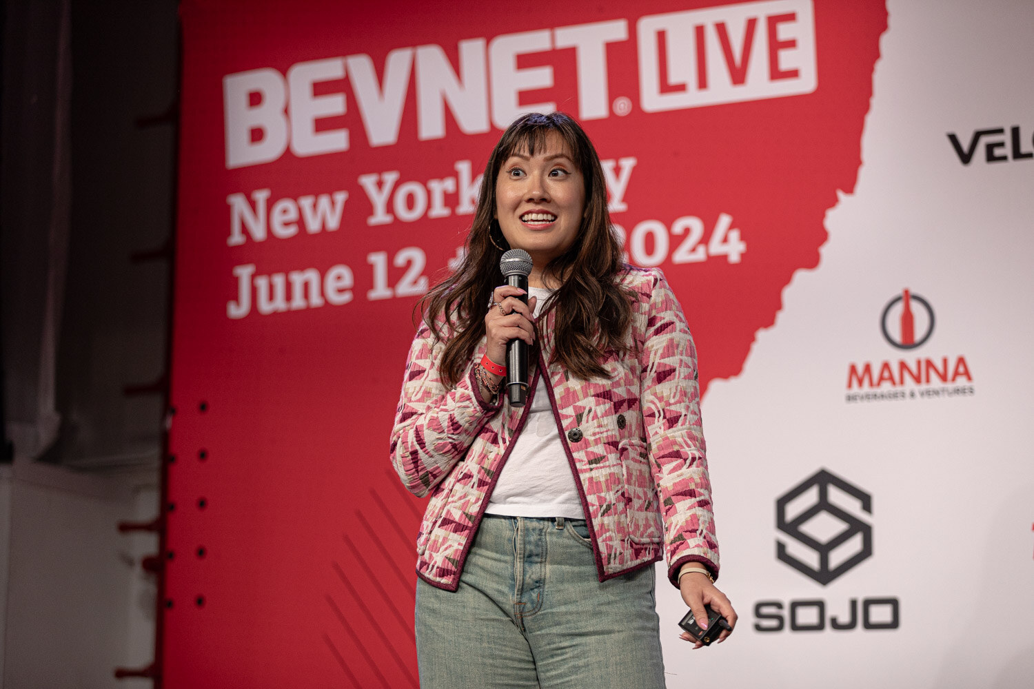 Finalist in a pink patterned jacket speaks in front of the BevNET Live backdrop.