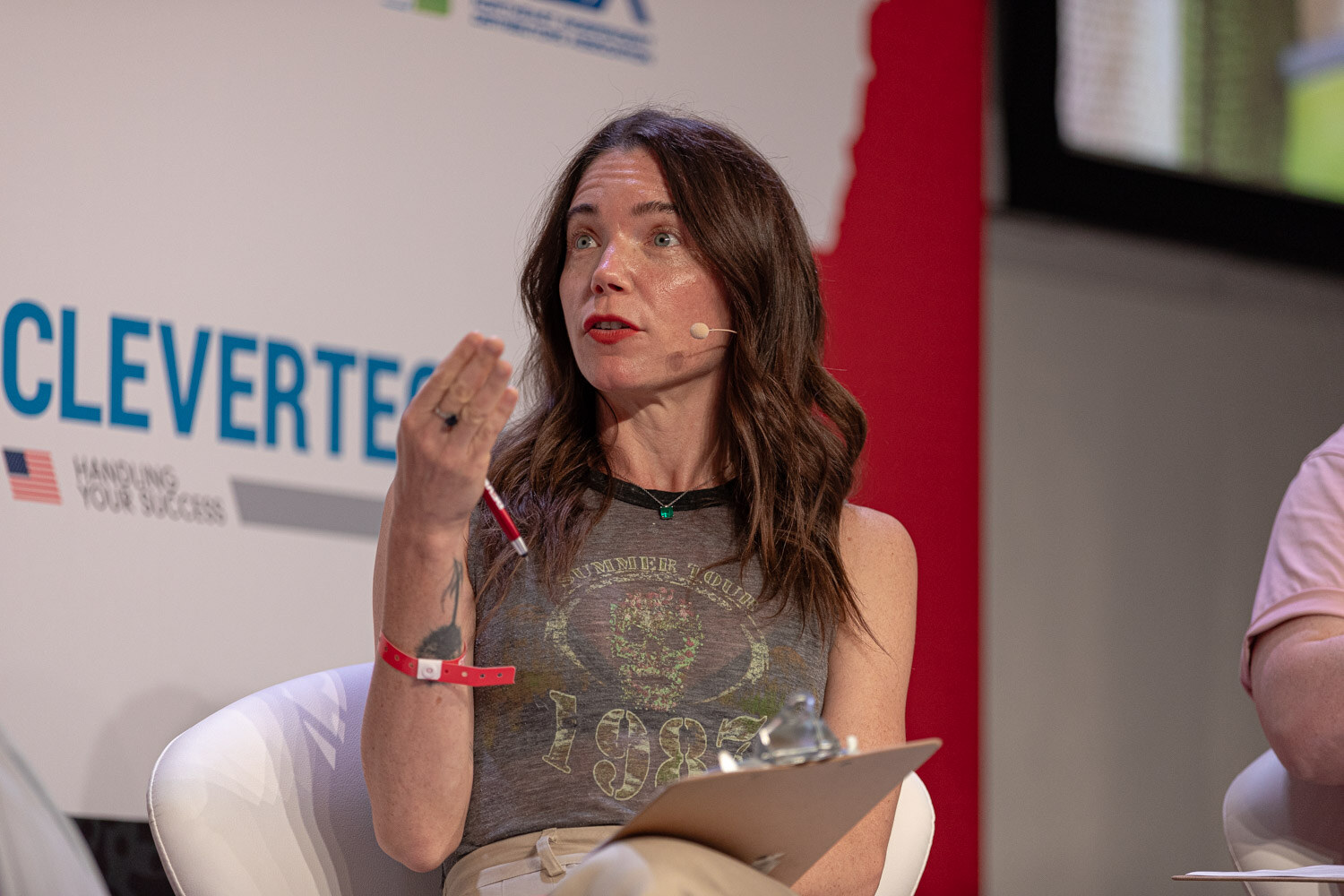 Judge in a graphic tank top holds a pen while speaking to the finalists.