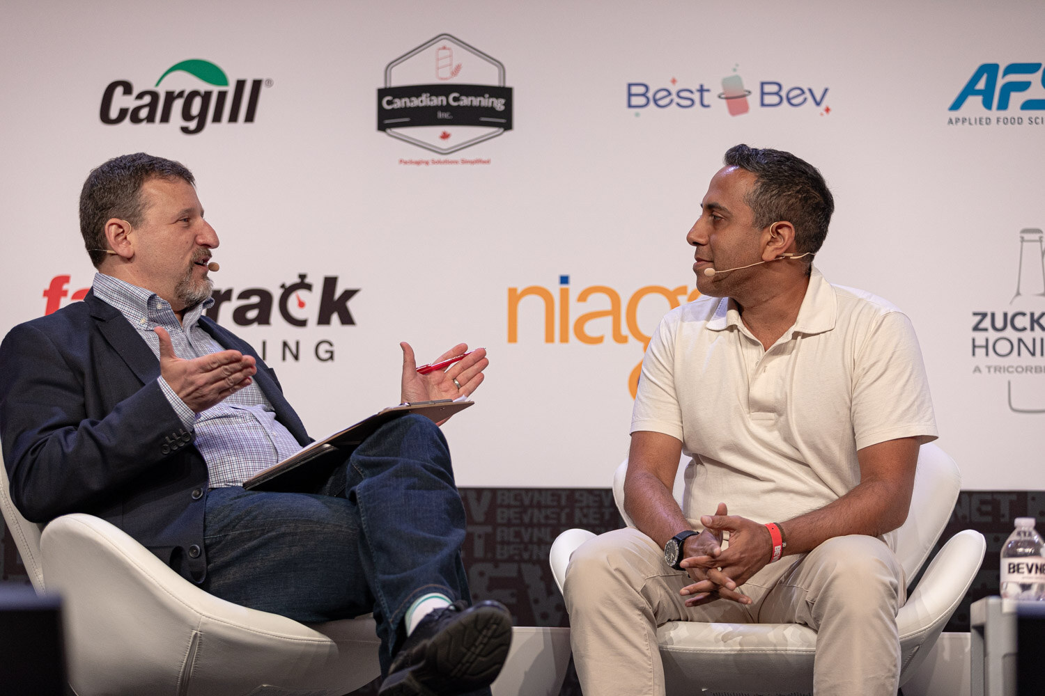 Moderator and a guest in a cream polo talk in white chairs during the Finance session.