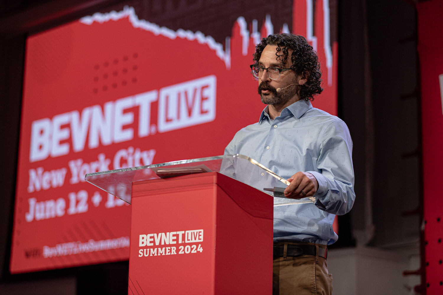 Moderator in a light blue shirt at the BevNET Live podium introduces the Building the Category session.