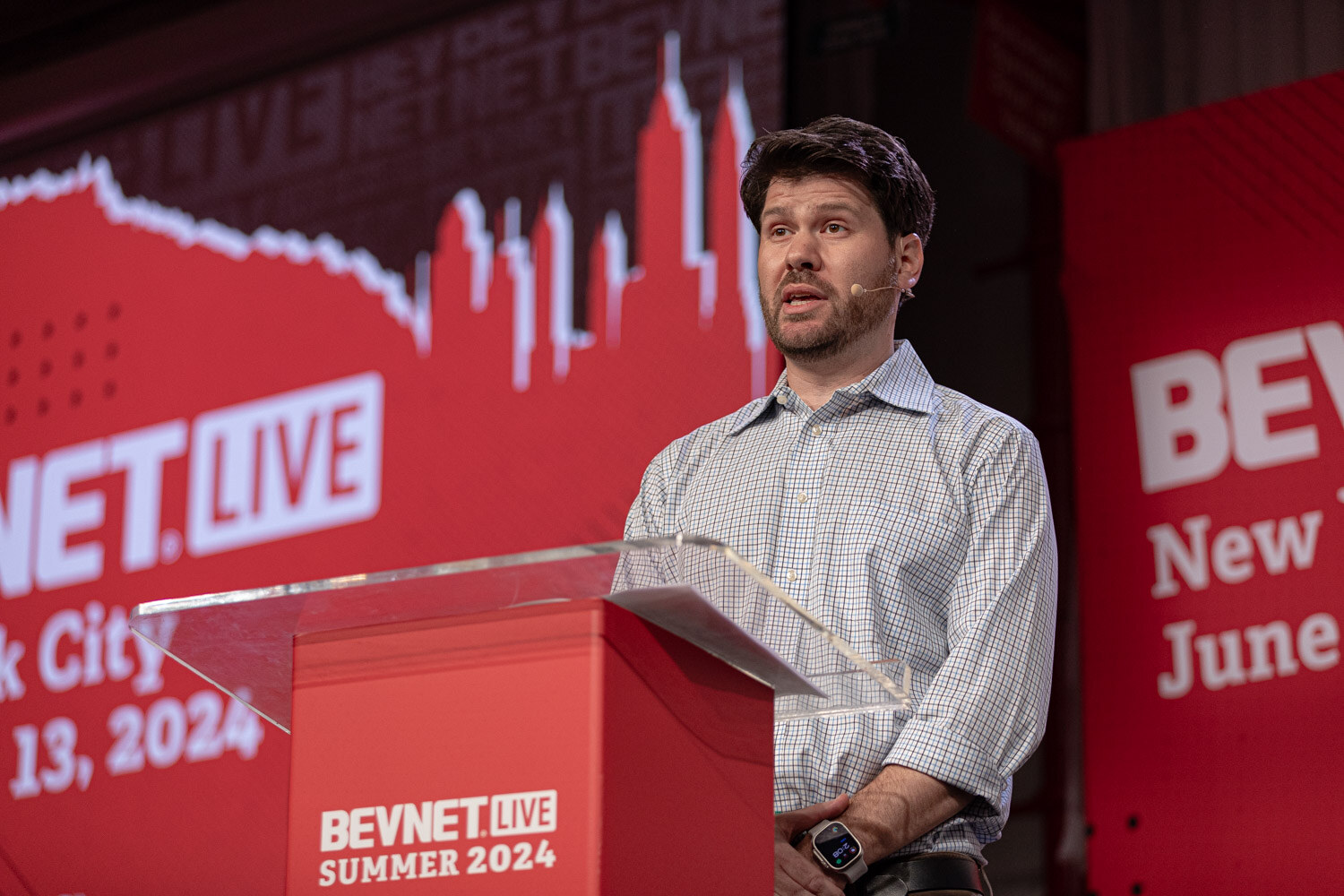 Moderator in a checked shirt at the BevNET Live podium opens the Sports Marketing session.