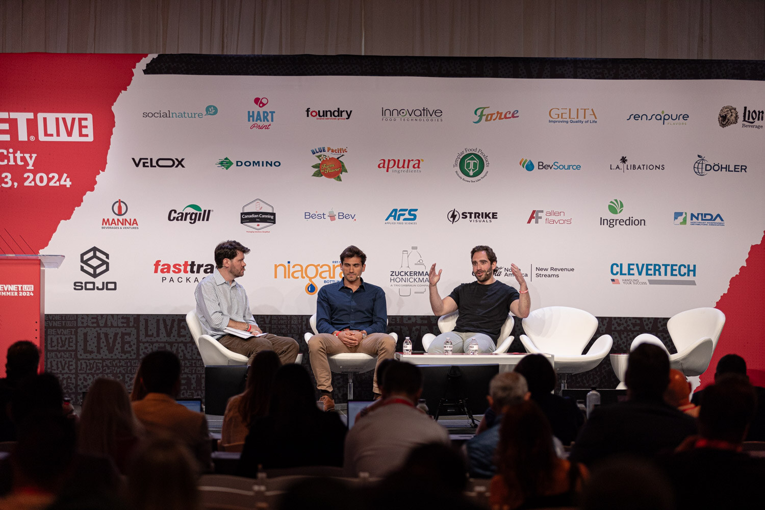 Wide view of the moderator and two panelists on the main stage in front of the audience.