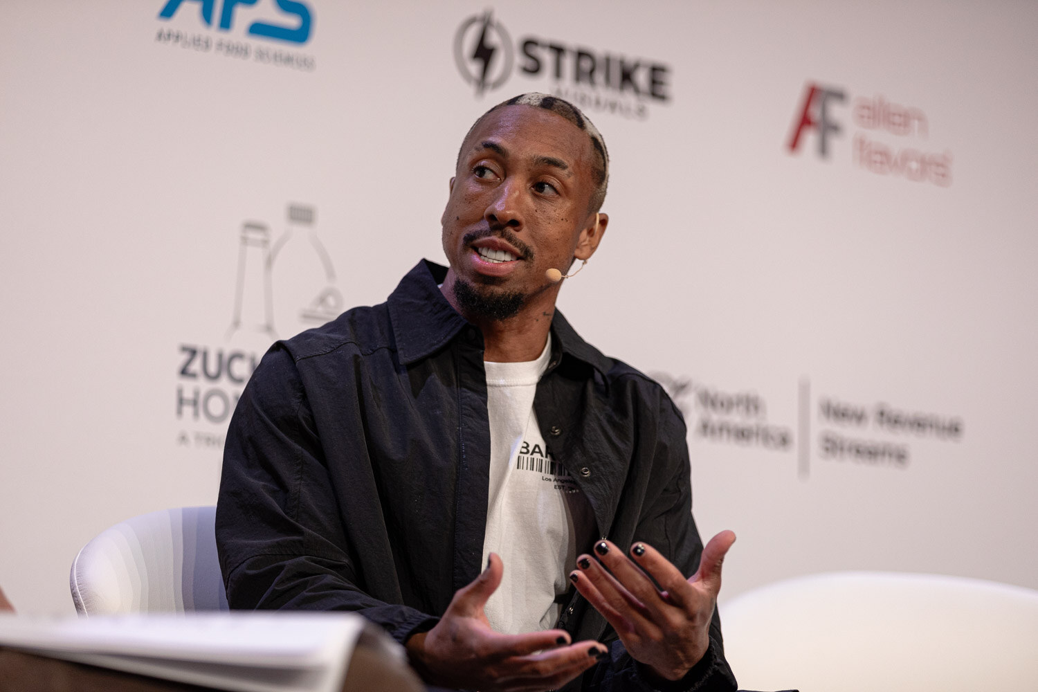 Guest in a black jacket answers a question with an open hand.
