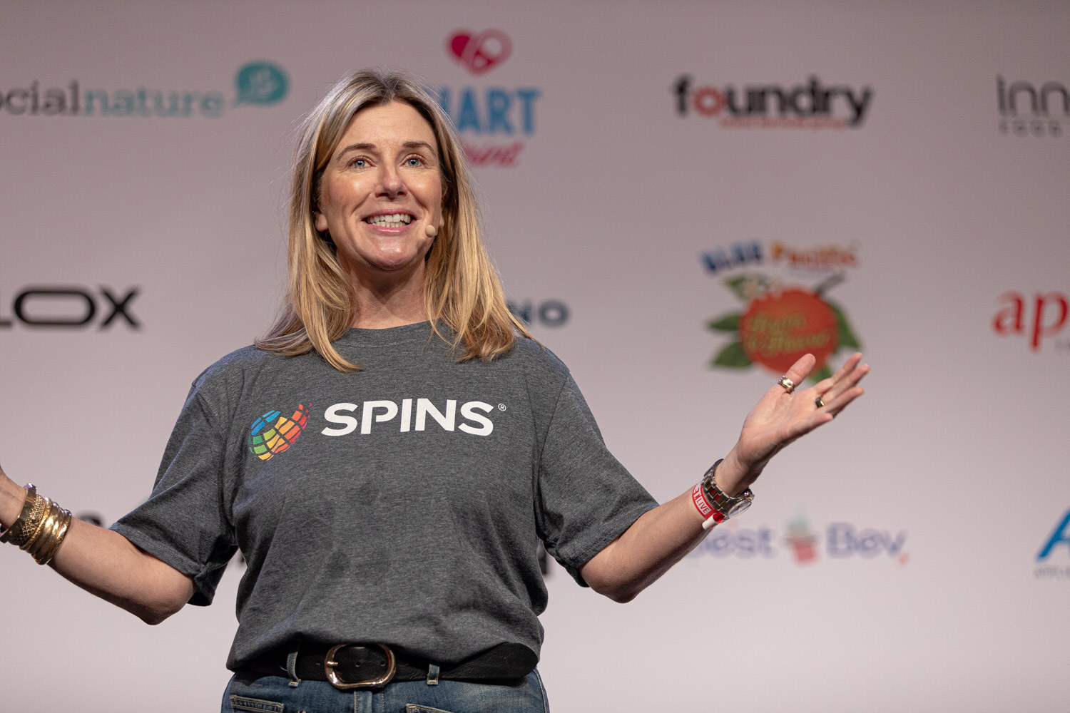 Speaker in a SPINS t-shirt smiles with arms open during Data Drive.