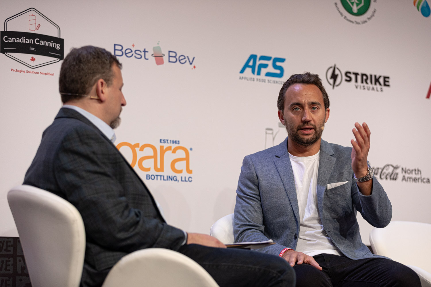 Moderator and guest in a gray blazer talk in white chairs during the Inside GoPuff session.
