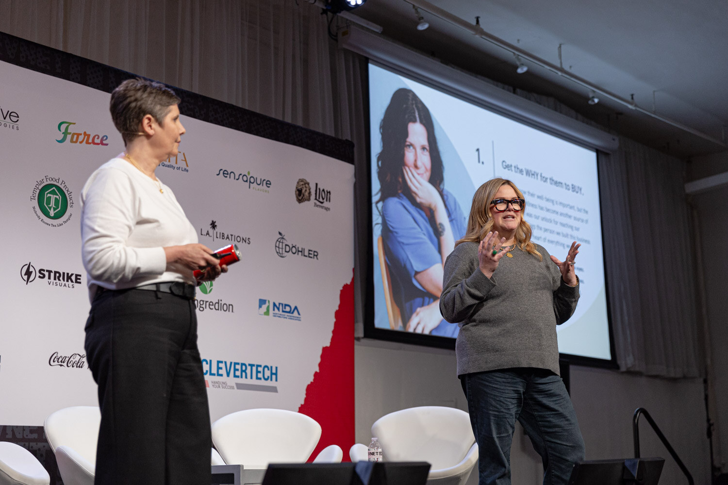 Two presenters on stage next to a slide numbered one about getting the why.